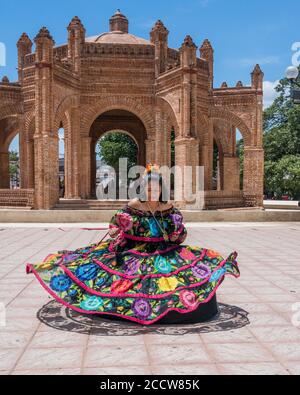 A young woman in the typical dance costume of Chiapa de Corzo poses in front of the La Pila fountain.  Chiapas, Mexico. Stock Photo