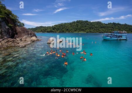 Tourist group snorkeling over coral reef with clear blue ocean water in tropical clear sea