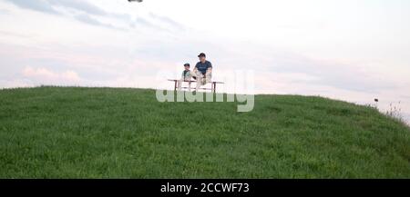 Father and son sitting together on a bench at the top of a hill. Rzeczyca Central Poland Europe Stock Photo