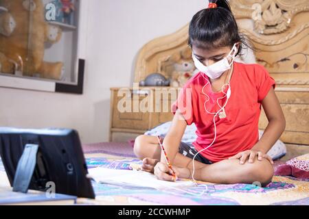 Indian schoolgirl student wearing mask studying online class with tablet at home, New normal.Covid-19 coronavirus.Social distancing, home schooling. Stock Photo