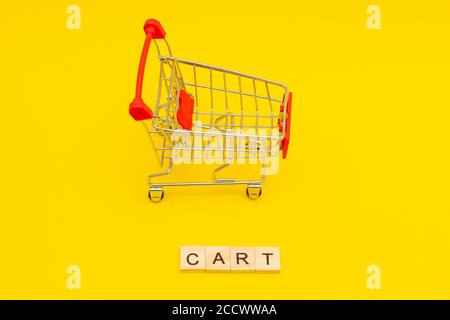 Word CART made from wooden cubes on yellow background with toys shopping cart Stock Photo