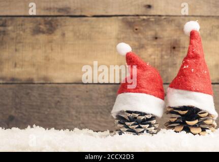 Two pine cones with Santa cap on snow, wooden background with space for text or image Stock Photo