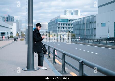 Young asian man waiting for bus and taxi on sidewalk Stock Photo
