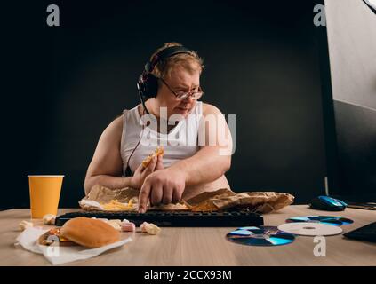 fat fair-haired freelancer in headphones working at home. man doing the shopping online. guy buying fast food from the net. business concept Stock Photo