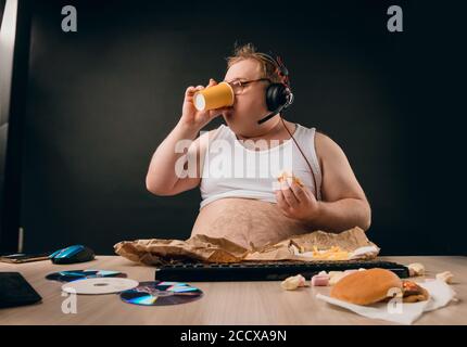 plump man with hairy stomach drinking coffee while using the computer. close up photo. isolated black background.weak willed man. guy holding a plasti Stock Photo