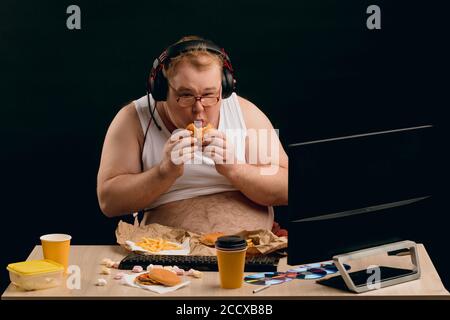 emotional funny guy enjoying fast food during using the computer .man having a break while playing online games. close up portrait. isolated black bac Stock Photo