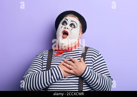 romantic clown with wide open mouth looking up, touching his heart with palms singing opera, gesturing with hands. funny guy performing a pantomime.is Stock Photo