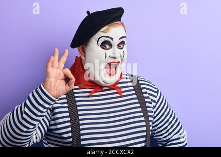 funny fat man in stiped sweater and black beret expresses agreement. close up portrait, body language, facial expression. isolated blue background Stock Photo