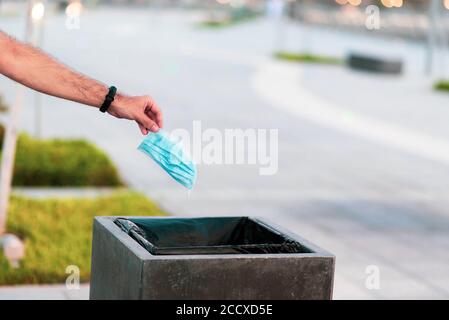 Man throwing used disposable protective surgical mask into the garbage bin closeup Stock Photo