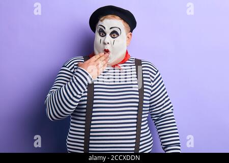 Shocked funny mime artist standing in disbelief closing his mouth with a palm isolated on blue background. close up portrait. studio shot.copy space Stock Photo