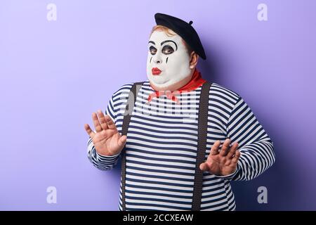 funny plump mime in stiped clothes asking not to worry, scared clown doesn't want to perform on stage Stock Photo