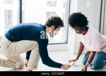 Mixed race couple of students, dressed in casual clothes, sit together on floor in well lit spacious room, prepare for upcoming exams, make project wo Stock Photo