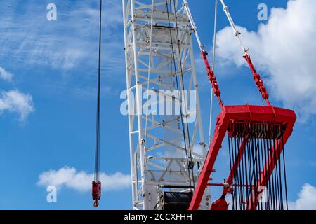 Crawler crane against blue sky and white clouds. Real estate industry. Red-white crane use reel lift up equipment in construction site. Crane for rent Stock Photo