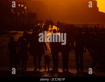 The sun sets as people walk along the footpath beside Cromer Beach, Norfolk. Stock Photo