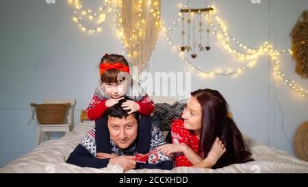playful daughter toddler sits on lying father shoulders and jumps having fun with parents on New Year eve at home closeup Stock Photo