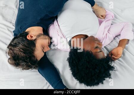 Close-up of happy interracial couple sleeping in bed together, enjoying the company of each other. Comfort and relaxation. Stock Photo