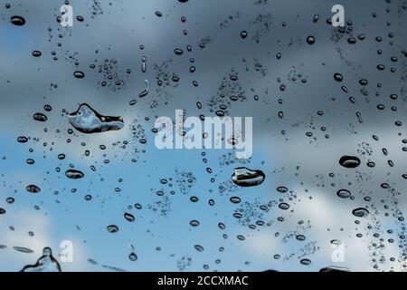 Macro abstract art view of water droplets on the glass windshield of an automobile with blue sky background Stock Photo