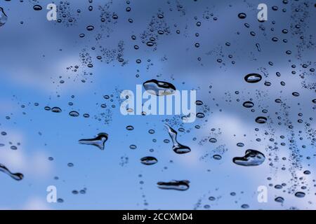 Macro abstract art view of water droplets on the glass windshield of an automobile with blue sky background Stock Photo