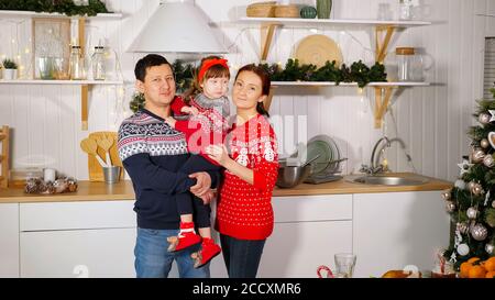 happy family in warm sweaters in New Year style poses for photoshoot against yellow garland in kitchen Stock Photo