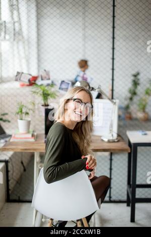 Portrait of a smiling young blond long-haired female student with blurred teachers and others in the classroom Stock Photo