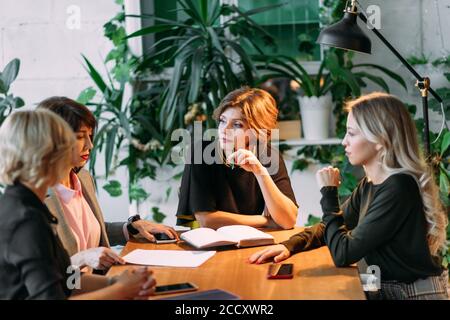 Group of younghardworking european young women working late at night in meeting room trying to complete their assignments. Stock Photo