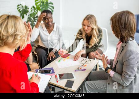 Brainstorming concept. Group of successful mixed race female entrepreneurs meet together to discuss future plans, make analysis, draw diagram on paper Stock Photo