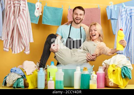 positive guy with his girlfriend in his hands posing to the camera in the laundry room. close up photo.careless life. many bottles in the foreground o Stock Photo