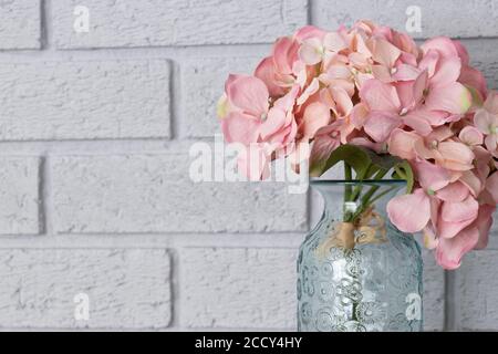 Artificial pink bunch of Hydrangea flowers in a glass vase.  Grey brick background Stock Photo