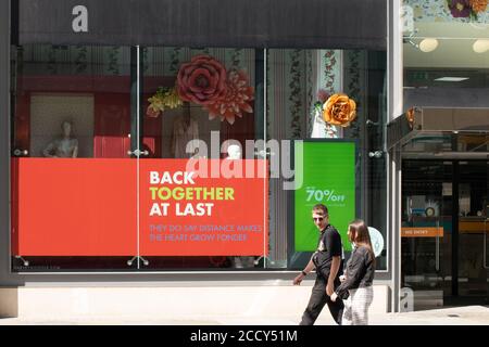 Harvey Nichols Manchester, UK. Shop window advertising Back Together at Last and 70% off with couple walking past. Stock Photo