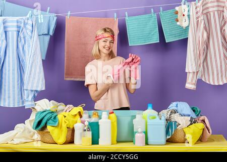blonde woman in pink t-shirt taking off her pink protective gloves after washing by hands. close up portrait. isolated blue background Stock Photo
