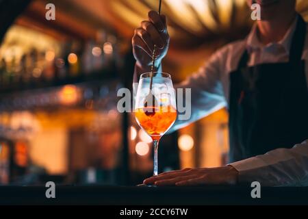 Barman hand stirring a fresh and sweet orange summer cocktail with a spoon on the bar counter. Stock Photo