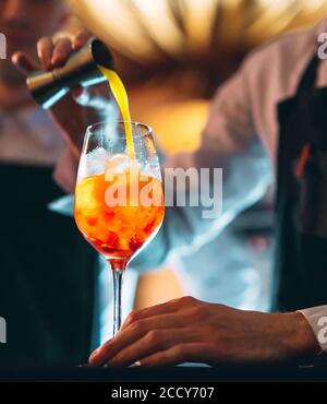 Barman hand stirring a fresh and sweet orange summer cocktail with a spoon on the bar counter. Stock Photo