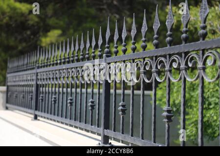 Black iron wrought fence of a park with ornate design. Stock Photo