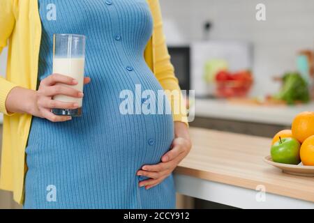 Young pregnant woman with glass of milk standing at kitchen Stock Photo
