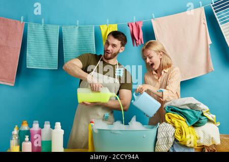 positive young couple with bottles of washing soap posing to the camera, cheerful family doing laundry. isolated blue background. studio shot.lifestyl Stock Photo