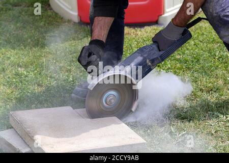 Worker using an angle grinder which is a handheld power tool to cut bricks at a construction site Stock Photo