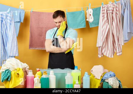 Stressed unhappy man with hand on his cheek having a rest while doing housework,bearded guy has problems while doing laundry. hanging wet clothes on t Stock Photo