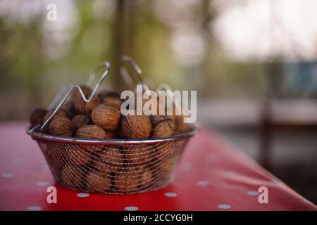 Mesh bowl full of walnuts on a red tablecloth with white dots Stock Photo