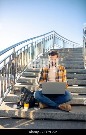 Young man in glasses with laptop on stairs outdoors Stock Photo