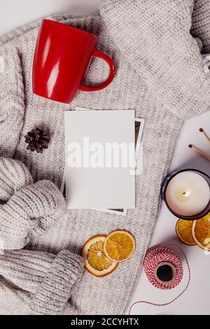 Flat lay of seasonal decor. Red cup, knitted sweater, candle and empty paper card. Stock Photo