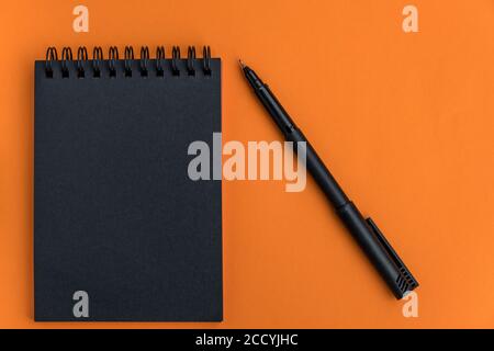 Black blank notebook and pen on an orange background. Minimalistic halloween celebration design. Mock up. Flat lay. Top view, space for text. Stock Photo