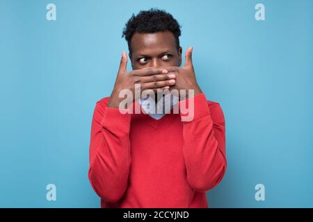 A scared young man is covering his face and is looking though his ...