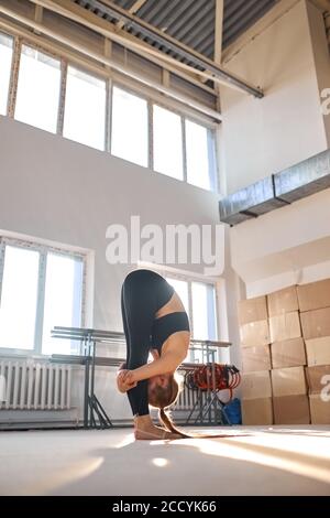 Sporty beautiful young woman doing gymnastics excersises , intense stretch, standing forward bend pose, working out wearing black sportswear, studio, Stock Photo