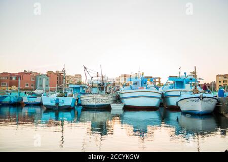 Egypt, Hurgada fishing boats on pier with city buildings on background at summer sunset Stock Photo