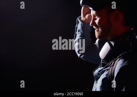Young man isolated over black background, stand with VR weapon, look side Stock Photo