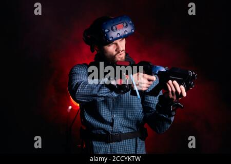 Young male wearing special devices for virtual reality games, isolated over red smoky background. Hi-tech Stock Photo