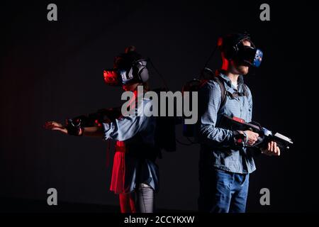 Man and woman wearing special goggles for vr futuristic games, stand don't looking at each other, in search with outstretched arms. Isolated over blac Stock Photo