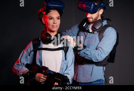 Young caucasian man and woman stand isolated on black background, using modern technologies, hi-tech. Virtual reality games Stock Photo