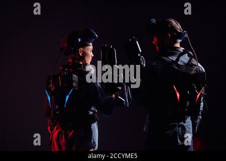 Man and woman stand opposite each other, holding vr weapons, team in virtual reality game. Isolated over black background Stock Photo