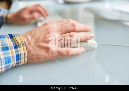 Hand of a senior operating computer mouse and keyboard on the computer Stock Photo